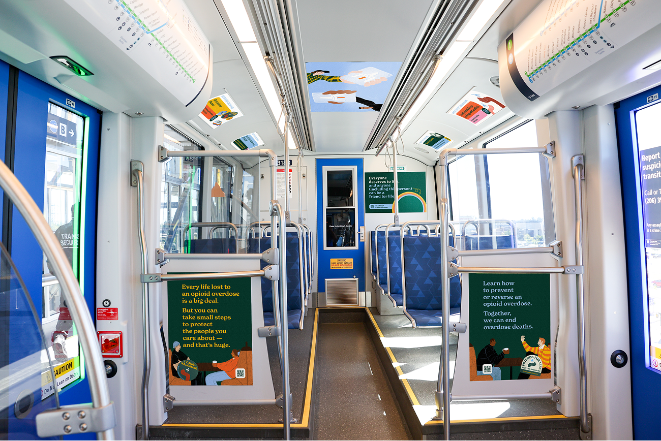Bright interior of a light-rail car covered with colorful Friends for Life overdose-prevention posters on the doors, walls, and ceiling.