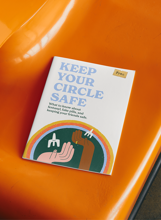 Keep Your Circle Safe” fentanyl-safety zine resting on a bright orange chair, with illustrated hands beneath a rainbow on the cover.