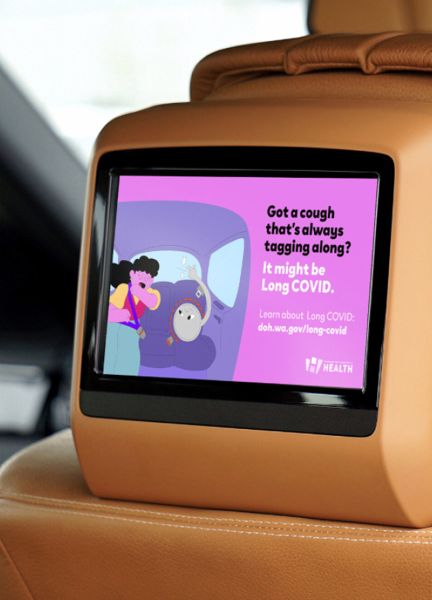 A picture of an ad on a screen behind the headrest of a car seat. The ad reads “Got a cough that’s always tagging along? It might be Long COVID. Learn about Long COVID: doh.wa.gov/long-covid.” The image on the billboard is an illustration of a woman sitting in the back seat of a car. She is coughing into her elbow. A creature representing Long COVID sits next to her, snapping its fingers to make her cough.